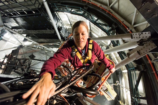 Emily M, an engineer, works on the telescope from a lift bucket in a harness.